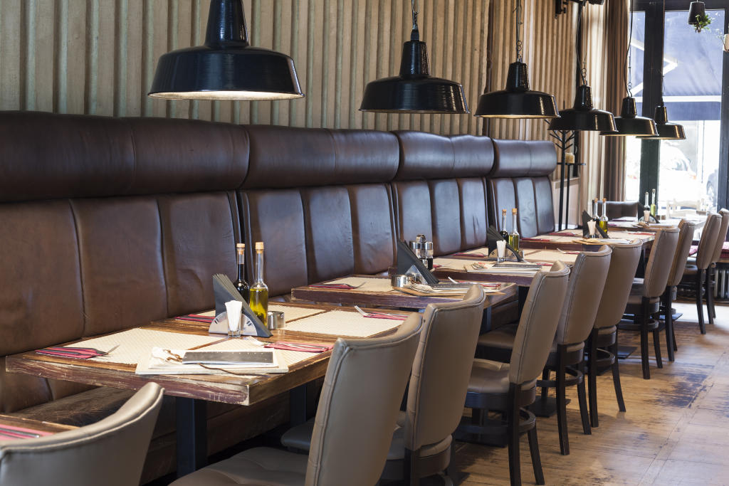 Modern restaurant interior with leather seating, elegant table settings, and pendant lighting, reflecting the precision and ambiance emphasized in Coyle Hospitality's dining services.